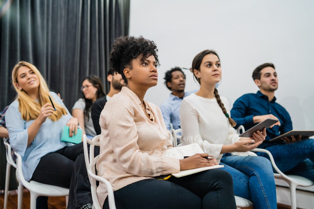 Pessoas sentadas em cadeiras, atentas e fazendo anotações, representando moradores de um condomínio durante uma assembleia para eleição de síndico.