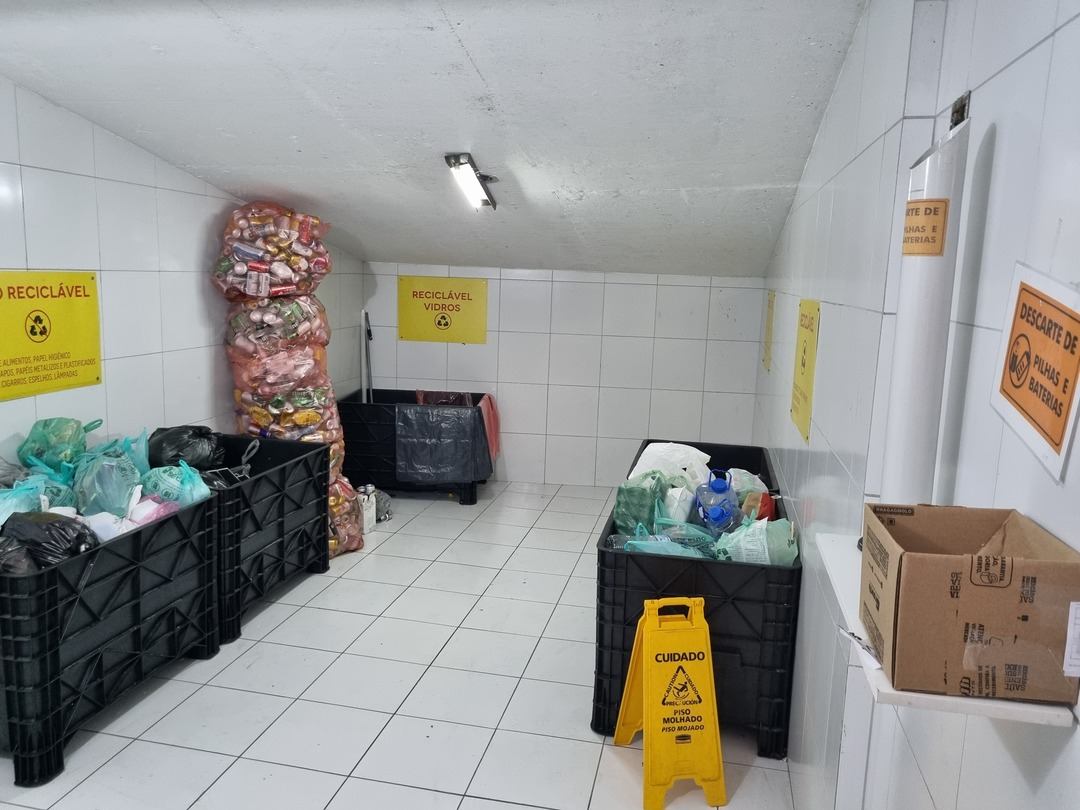 Área interna de um condomínio com recipientes para coleta seletiva de recicláveis, vidros e pilhas, ilustrando artigo sobre como gerar receita para o condomínio