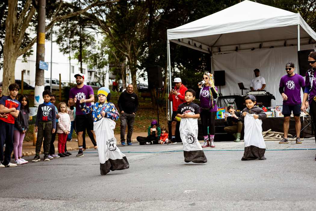Crianças participam de uma corrida de saco em evento ao ar livre, acompanhadas por adultos e animadores sob uma tenda, em clima de diversão e integração, ilustrando artigo sobre o que é gestão de condomínios