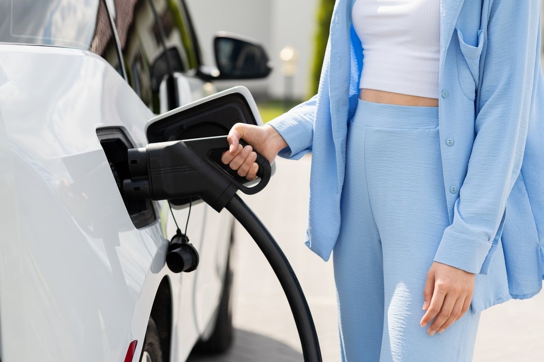 Mulher conectando carregador ao carro, simbolizando a expansão dos veículos elétricos em condomínios e a necessidade de instalações seguras