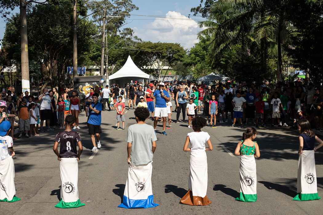 Crianças participando de uma atividade recreativa de corrida do saco em uma rua fechada para evento comunitário, com moradores e famílias ao redor observando e interagindo, ilustrando artigo sobre impacto social em condomínios.